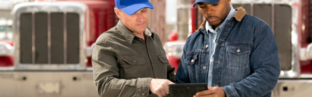 two men looking at tablet in front of semi truck