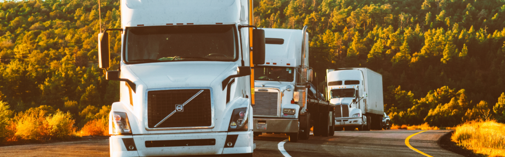 white volvo semi truck followed by other semi trucks