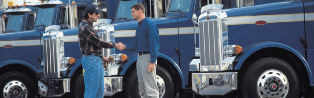 two men shaking hands in front of semi trucks