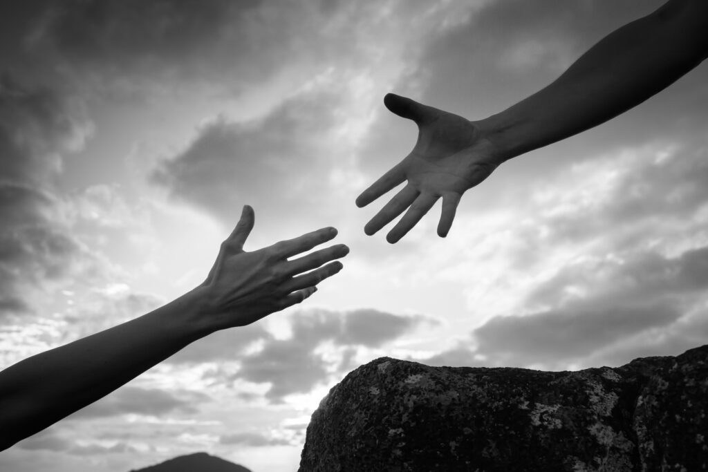 Hand helping another up a mountain path.