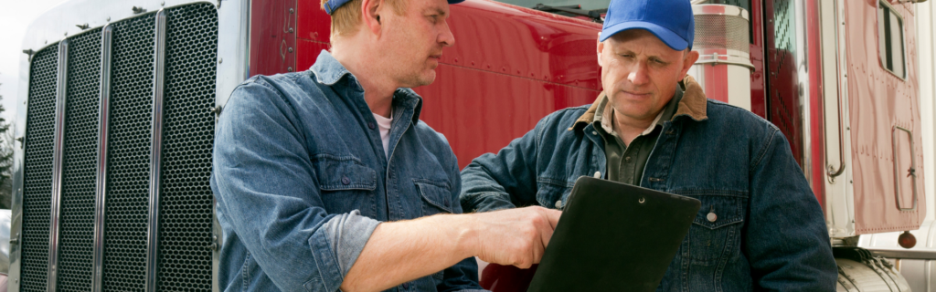 two men looking at clipboard in front of semi truck