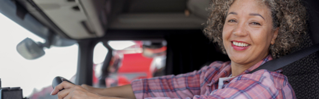 black woman in pick plaid shirt driving semi truck