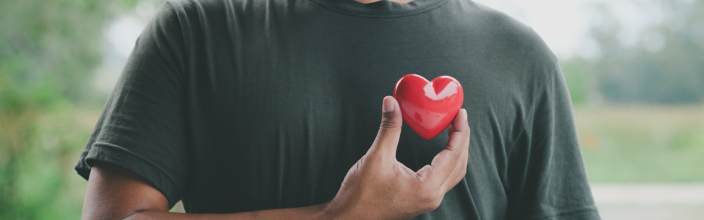 man in gray t-shirt holding red heart up over chest