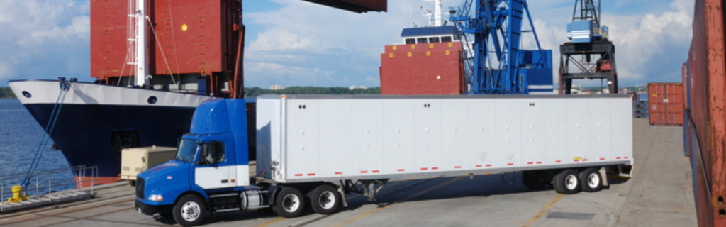 semi truck at port with cargo ship and crane in background