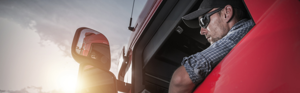 Man wearing hat and sunglasses in cab of red semi truck