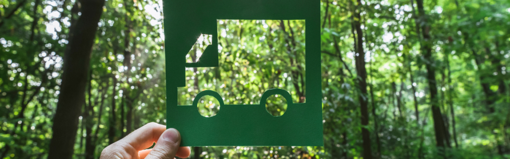 hand holding up cutout of truck in front of a forest of trees