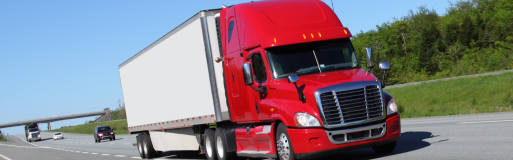 red semi truck with white trailer driving on road with bridge and trees in background